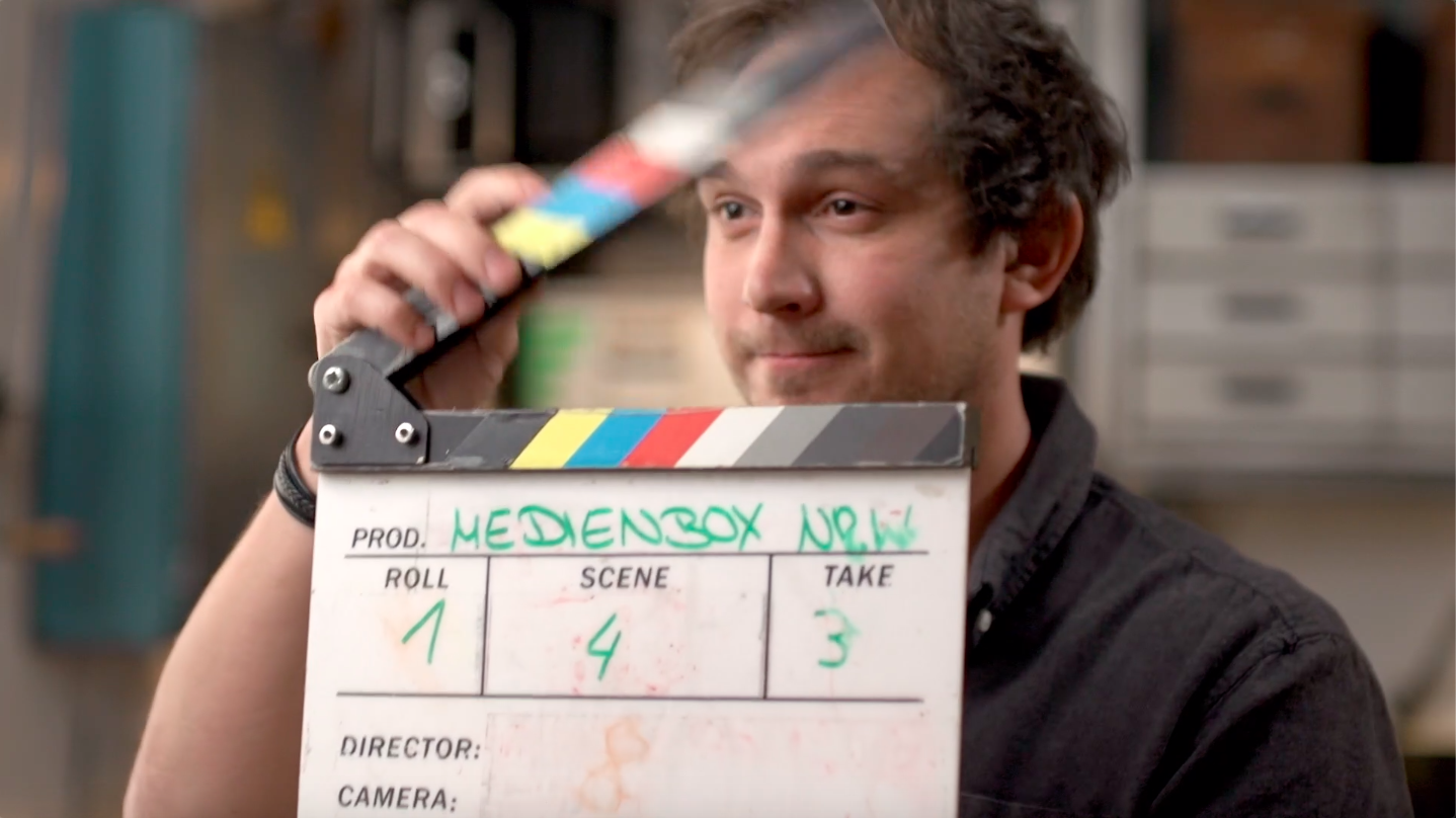 Bild eines Mannes mit einer Filmklappe aus dem Modul Videos schneiden: Bildbearbeitung für Fortgeschrittene von der Medienbox NRW